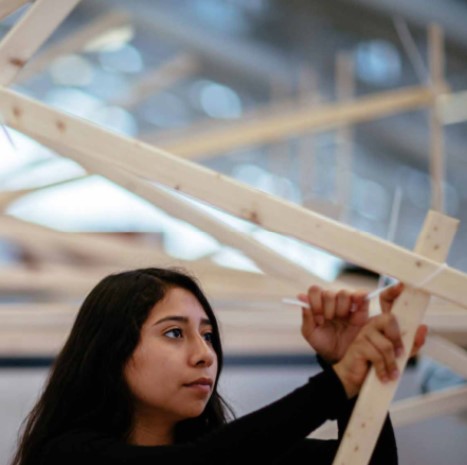 Image of a Design Discovery Youth participant constructing a physical model out of lumber members inside Gund Hall at Harvard's Graduate School of Design.  