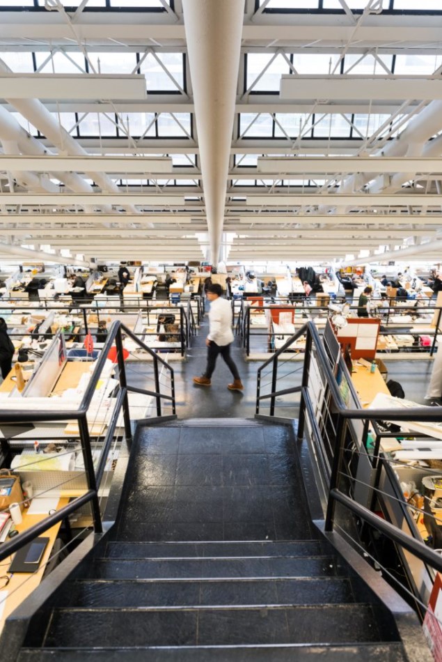 An image of the inside of Gund Hall at Harvard's Graduate School of Design looking down the studio trays along an interior stairway.  A design student is walking along the floor level below.  