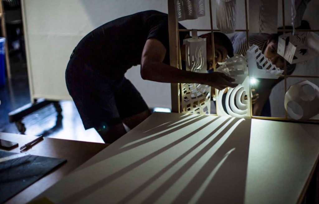 Image of a Design Discovery Youth participant arranging paper models to photograph in a darkened space.  