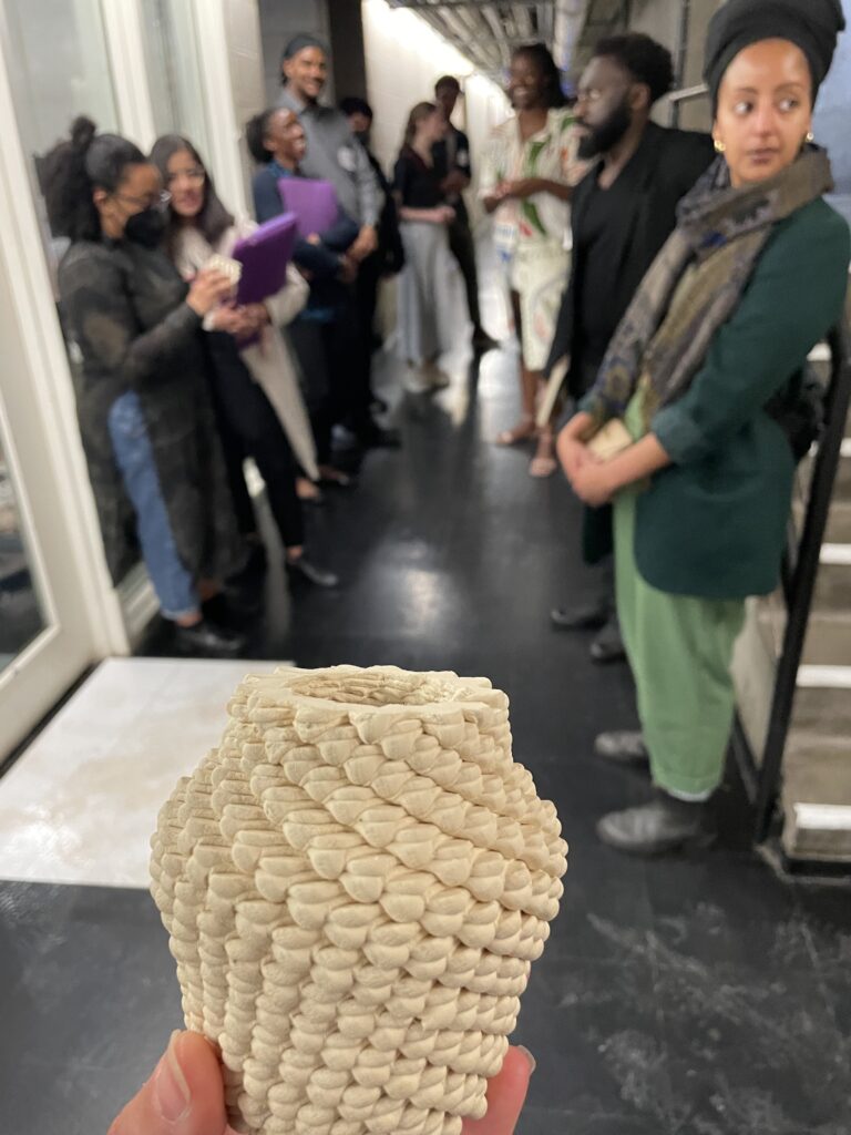 Image of the program participants touring the Harvard Graduate School of Design's fabrication laboratory.  A 3D cast model is held up in front of the full group of students and mentors standing in the school.  